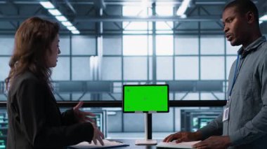 Mühendisler sunucu odasını model cihazıyla denetliyor, donanım belgelerini okuyor. Ekip sunucu merkezinde inceleme yapıyor, yeşil ekran tableti ile ilgili teknik dosyaları okuyor, kamera A