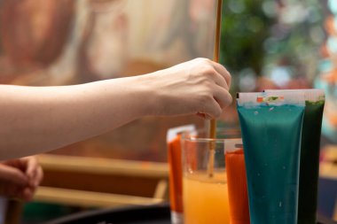 Ressam, güzel bir başyapıt çizmek için sanatsal malzemeler ve fırçalar kullanarak tuval üzerinde bir sanat eseri yaratmak için suluboya tüpleri kullanıyor. Yaratıcılık ve ilham dolu bir ressam. Kapat..