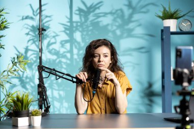 Stüdyoda canlı yayın yapan Streamer, üç ayaklı akıllı telefon ve mikrofon kullanarak canlı ses ve görüntü kalitesini sağlama alıyor. İnternet yıldızı profesyonel mikrofona konuşuyor, takipçilerle konuşuyor.