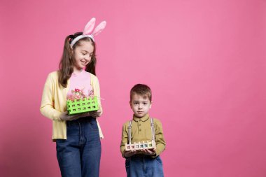 Kamerada neşeli renkli dekorasyonlar gösteren sevimli kardeşler, Paskalya kutlaması ve bahar zamanı için heyecanlanıyorlar. Erkek ve kız kardeşler boya dolu sepetlerini sunuyorlar..