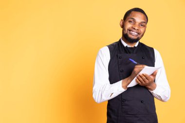 Önlüklü yetenekli garson müşterilerden yemek siparişlerini not defterine alır müşteri memnuniyeti için önemli bilgiler yazar. Hizmet sektöründe çalışan kahya.