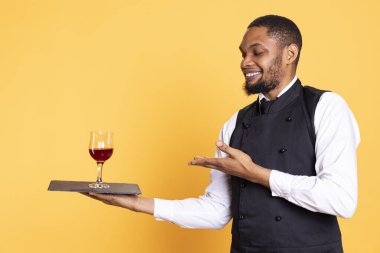 Restaurant worker serving people with a glass of red wine before dinner, recommending a special drink for customer satisfaction. Waiter carrying a tray for a taste test, professionalism. clipart