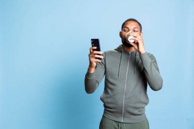 Afro-amerikan adam mesajlarını kontrol ediyor, kahve servisi yapıyor, kafein içkisini içiyor ve web sitelerini karıştırıyor. İnternette gezinen ve mesajlaşan genç kişi.