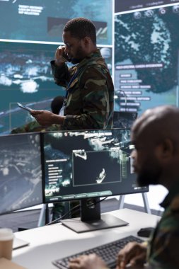Çağdaş bir kontrol odasında telefon görüşmesi yapan bir asker gerçek zamanlı verileri işliyor ve gözetim çabalarını koordine ediyor. Karar verme süreçlerini destekleyerek ulusal güvenliği artırmak.