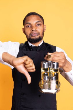 Professional waiter showing a thumbs down symbol in studio, showing his disapproval and being dissatisfied on camera. Restaurant employee gives a dislike, negative vibes. clipart