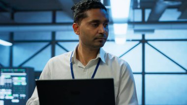 Veri merkezindeki sistem yöneticisi, en iyi performans ve güvenilirliği sağlamak için dizüstü bilgisayar kullanarak ekipmanları tasarlar, uygular ve yönetir. Sunucu odasındaki Hintli adam dizüstü bilgisayarda kodluyor, kamera A