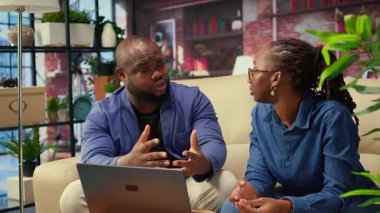 Kanepedeki Afrikalı Amerikalı genç serbest çalışanlar modern teknoloji ve araçları kullanarak trendleri analiz ederek ve başarıyı artırarak bir iş fikrini paylaşıyorlar. Çift iş akışını verimli bir şekilde geliştiriyor. Kamera A.