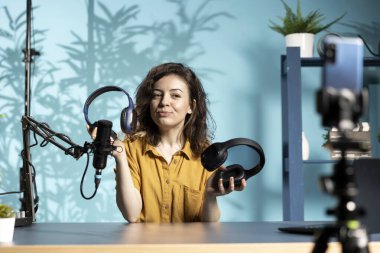 Yeni piyasaya sürülen kablosuz kulaklıkları gözden geçiren işitme hastası akıllı telefon kamerasıyla çekim yapıyor. Teknoloji uzmanı telefon kullanarak internet kanalı videosu kaydediyor, dinleme aygıtı özelliklerini kontrol ediyor