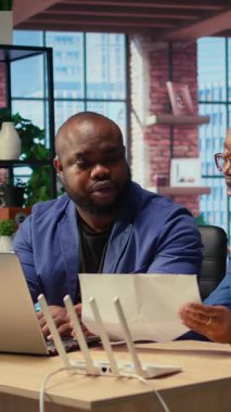 Merkez ofisteki Afro-Amerikalı çift Wi-Fi modemlerini bozuyor ve uzaktan çalışma verimliliklerini etkileyen zayıf bağlantıyı düzeltmek için çözümleri tartışıyorlar. Yönlendirici kılavuz dosyaları. Kamera A.