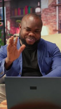 Siyahi genç bir çift evlerinde video bağlantısı kuruyor, kanepede oturuyor ve arkadaşlarıyla konuşuyor. Kadın ve erkek video konferansında el sallıyor, yaşam tarzı. Kamera A.