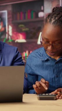 Afrikalı Amerikalı çift, ev kredisi ve sigorta ödemelerini ev bütçesi ve para yönetimi için hesap makinesi kullanarak tartışıyor. Güvenli bir finansal geleceği garantiye almak. Kamera A.