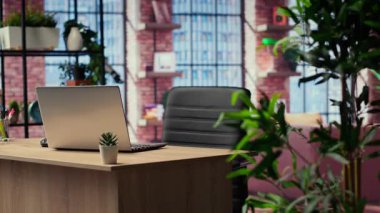 Uzak bir iş için ev ofis masası, şık mobilya ve kapalı mekan bitkileriyle dekore edilmiş modern bir apartman dairesi. Ahşap zeminli boş stüdyo alanı.