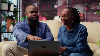 Oturma odasındaki siyah çift, modern teknolojiyi trendleri araştırmak ve verimliliği artırmak için kullanarak, online bir iş için yaratıcı fikirleri tartışıyor. Motivasyon ve başarı için destek. Kamera B.