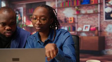 Bağımsızlar rapor kağıtlarından veri girerek hesap tablolarını dolduruyorlar, ay sonunda rakamları analiz ediyorlar. Afrika kökenli Amerikalı erkek ve kadın evden çalışıyor. Kamera A.