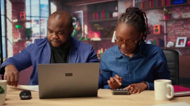 Afrikalı Amerikalı çift, ev kredisi ve sigorta ödemelerini ev bütçesi ve para yönetimi için hesap makinesi kullanarak tartışıyor. Güvenli bir finansal geleceği garantiye almak. Kamera A.