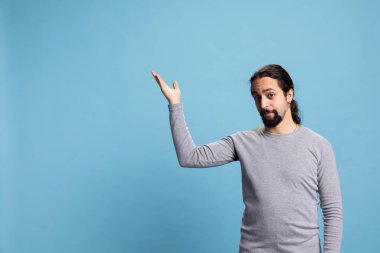 Orta Doğulu bir adam kameranın önündeki yönü gösteriyor, sağ ya da sol taraftaki bir şeyi mavi arka plana işaret ediyor. Genç yetişkin reklam yapıyor..