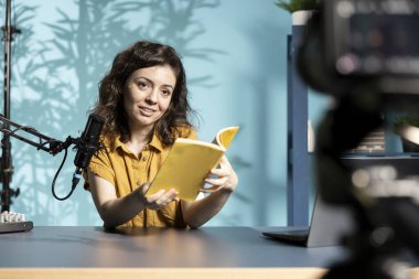 Stüdyodaki gülümseyen nüfuzlu yayınevinin yeni çıkan ciltli kitabını eleştiriyor. Yazardan okuyucuya yeni bir roman sunan mutlu akademisyen edebiyat videosu denemesi çekiyor