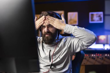 Angry man playing videogames, feeling headache from stress after being defeated by enemies. Competitive pro gamer unable to believe his eyes after failing to win online multiplayer esports match clipart