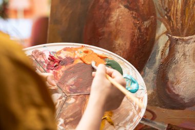 Güzel sanatlar atölyesinde yarattığı sanat eseri için suluboya boya boya kullanan ve paletteki renkleri karıştıran kadın sanatçı. Tuvale kırsal öğeler çizen bir kadın, atölyede yaratıcı bir süreç. Kapat..