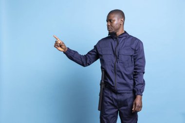 Güvenlik görevlisi üniformalı Afro-Amerikan bir adam sol tarafı işaret ediyor, yanında bir şey sunmak için reklam yapıyor. Ajan işaret parmağını kaldırıyor, yönü gösteriyor..