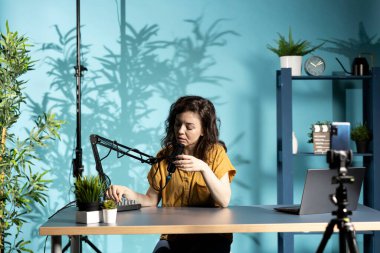 Etkilendirici ses karıştırıcıyı çalıştırıyor, mikrofonun yaklaşan video için temiz ses yakalamasını sağlıyor, selfie cep telefonu kamerasıyla çekim yapıyor. Kadın ses seviyelerini kontrol ediyor, cep telefonuyla kayıt yapıyor.