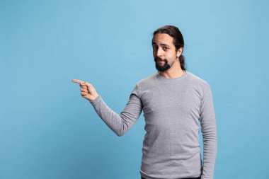Stüdyonun sol ya da sağ tarafındaki bir şeyi işaret eden kendine güvenen adam mavi arka planda bir reklam yaratıyor. Genç yetişkin kameranın yönünü gösteriyor..