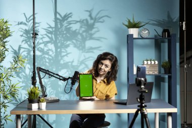 Teknoloji mühendisi, düşük bütçe aralığında izole ekran tableti sunuyor, loş ışıklandırılmış ev stüdyosundan. İçerik oluşturucu çevrimiçi izleyiciler önünde dijital aygıtı gözden geçiriyor