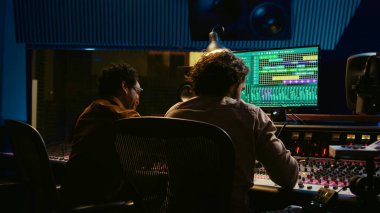 Sanatçı ve ses tasarımcılarından oluşan çeşitli bir ekip yeni bir hit için kurgu melodileri üzerinde çalışıyor, hareket eden faderler ve renkli sayaçlarla karıştırma konsolunu çalıştırıyor. Müzisyen ve yapımcı şarkılar yapıyor. Kamera B.