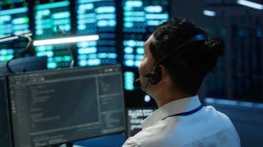 Veri Merkezi bilgisayar bilimcisi mikrofon takıyor, ağ donanımı kuruyor. Sunucu merkezi IT çalışanı sistem yöneticileriyle mikrofonla konuşuyor, kamera A