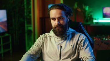 Profesyonel oyuncu, son teknoloji oyun sistemini kullanarak online çok oyunculu turnuvaya katılıyor. RGB ışıkları altında odaklanmış bir adam oturma odasını aydınlatıyor ve video oyunları oynuyor.