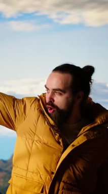 Dikey Video Heyecanlı Gezgin, dağın zirvesine tırmanıp doğanın panoramik güzelliğinin tadını çıkararak zafer kazanarak kollarını kaldırıyor. Uçsuz bucaksız gökyüzüne ve uçsuz bucaksız manzaraya hayranlık duyuyorum.