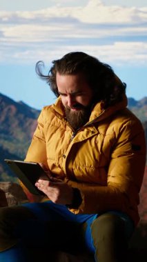 Dikey Video Camper, yüksek irtifada bir kamp alanında tablet kullanarak daha iyi sinyal arayarak ve güvenliğini riske atarak güçlü bir rüzgarla savaşıyor. Tehlikeli dağ sıraları soğuk hava. Kamera B.