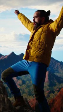 Dikey Video Trekker, kollarını dağ sırasının tepesinde heyecan içinde uzatıyor, tırmanma başarısından gurur duyuyor ve tatmin oluyor. Genç yetişkinler azim ve hırslarını sergiler.