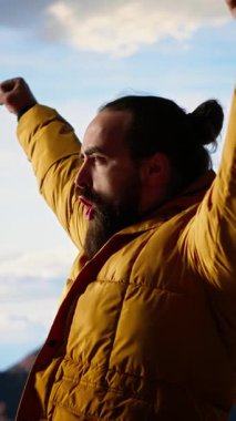 Dikey Video Trekker, kollarını dağ sırasının tepesinde heyecan içinde uzatıyor, tırmanma başarısından gurur duyuyor ve tatmin oluyor. Genç yetişkinler azim ve hırslarını sergiler.