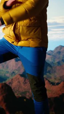 Dikey Video Yürüyüşçüsü bir dağın zirvesinde zaferle duruyor. Kollarını zaferle kaldırarak kişisel başarısını başarılı bir tırmanışla kutluyor. Manzaralı manzara ve özgürlük için sonsuz gökyüzü. Kamera A.