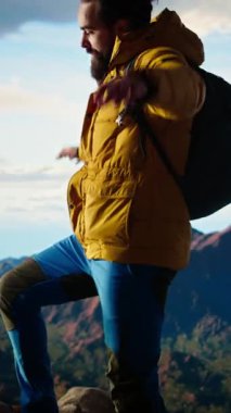 Dikey Video Erkek Yürüyüşçüsü, vahşi doğaya hayran kalarak, temiz dağ havasından derin bir nefes alır. Nefes kesici manzara farkındalık ve rahatlamaya ilham verir. Kamera.