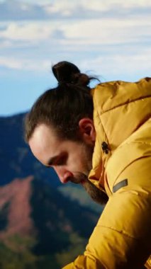 Dikey Video Erkek Yürüyüşçüsü, tepenin zirvesinden nefes kesici bir dağ sırasına bakar ve büyük açık havanın yalnızlığını ve temiz havasını kucaklar. Macera hissi ve sonsuz doğa keşfi.