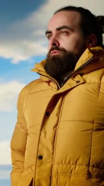 Dikey Video Doğa Aşığı nefes kesen bir dağ sırasının kenarında duruyor, yükselen zirvelerin ve engin gökyüzünün manzaralı arka planına bakıyor. Genç adam macera ve açık hava keşiflerini seviyor.