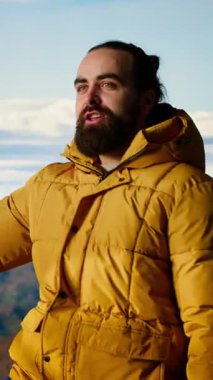 Vertical Video Male içerik yaratıcısı bulutlardaki dağ zirveleriyle çevrili bir video kaydediyor, bir dağ sıraları tepesine tırmanıyor ve sosyal medya izleyicileri için canlı yayın yapıyor. Maceracı ruh.