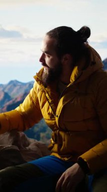 Dikey Video Kaşifi bir dağ zirvesine ulaşmanın heyecanını kucaklıyor ve rahatlatıyor, temiz havayı ve panoramik güzelliği hissediyor. Yürüyüşçü heyecanlı ve yorgun, kendini geliştirme ve hedeflerle gurur duyuyor