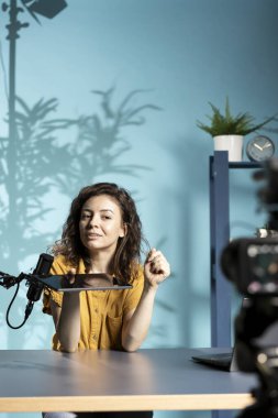 Yüksek teknoloji mühendisi düşük bütçeli tablet sunuyor, loş ışıklandırılmış ev stüdyosundan film çekiyor. Çevrimiçi izleyiciler önünde dijital aygıtı inceleyen neşeli teknoloji içeriği oluşturucu