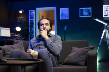 Tembel adam evde televizyon izlemekten ve patlamış mısır yemekten zevk alıyor. Aydınlatılmış apartman dairesinde kanepe patatesi, ağzına tuzlu atıştırmalıklar doldurmak, televizyonla eğlenmek.