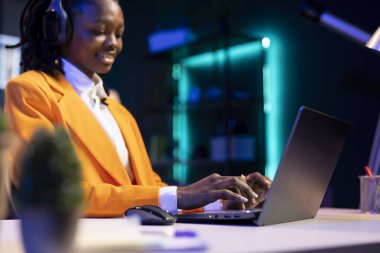 Şirket projesi için verileri araştırırken müziğin tadını çıkaran mutlu bir serbest yazar. Bir gecede kişisel ev ofisinde görevler yapıyor. Gülümseyen kadın masada oturuyor, dizüstü bilgisayarda yazıyor ve kulaklık takıyor.