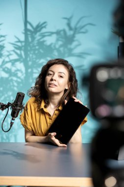 Teknoloji uzmanı, düşük bütçeli tableti ilgili izleyicilere profesyonel kamerayla sunuyor. Dijital aygıtı inceleyen kadın, özel ekipmanlarla kayıt yapıyor