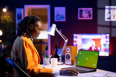 Merkez ofisteki kadın yeşil ekran laptopuyla yazı yazıyor, masada oturuyor. Afrikalı Amerikalı serbest çalışan, iş vardiyasına başlıyor. Model defteri kullanıyor, e-posta iletişimi yapıyor.