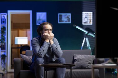 En sevdiği takımın kazanması için dua eden endişeli suratlı bir adam TV 'de canlı yayın yapan spor olayını izliyor. Evde tırnak yeme yarışmasına bakan endişeli bir destekçi