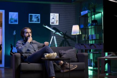 Kanepede oturmuş televizyon karşısında patlamış mısır yiyen kordon kesicisi canlı film gösteriyor. Evde atıştırmalık yiyen ve televizyondaki talep kanallarında video izleyen neşeli bir insan.