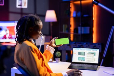 Merkez ofisteki serbest çalışan yatırımcı yeşil ekranlı telefondan video izlemek için dizüstü bilgisayardaki borsayı kontrol etmeye ara veriyor. Piyasa hisseleri artışına bakan akıllı telefonu tutan serbest çalışan.