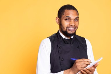 Profesyonel uşak, müşterilerin siparişlerini not defterine yazar, beş yıldızlı restoran müşterilerine hizmet etmek için not alır. Afrika kökenli Amerikalı garson önlük giyiyor, hizmet odaklı endüstri.