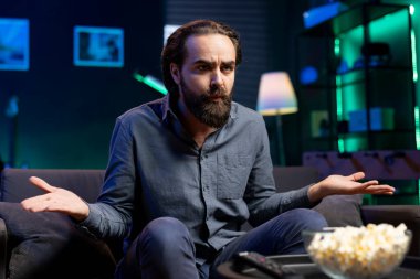 Kanepede oturmuş, karakterlere ters düşen abonelik temelli yayın hizmetleri üzerine gerilim serisi çekmek için TV 'yi kullanan şaşkın insan. TV 'de VOD programları izleyen bir adam entrikadan dolayı kafası karışmış.